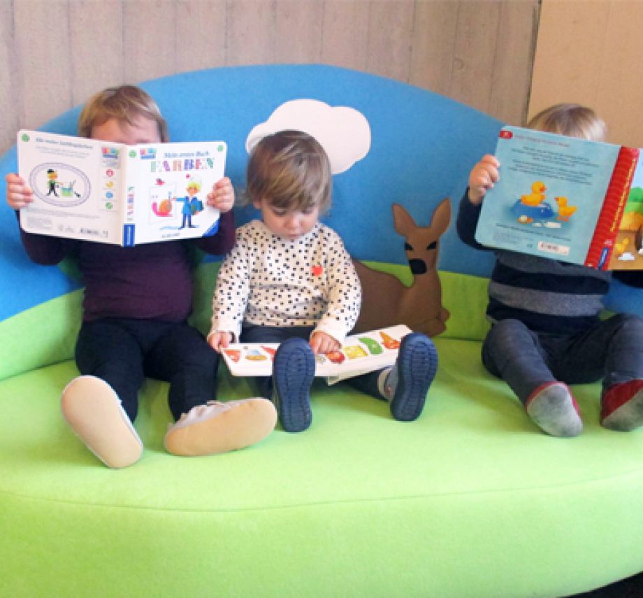 3 Kindergartenkinder lesen Bücher, auf Lesesofa grün mit Himmmel und Reh-Motiv